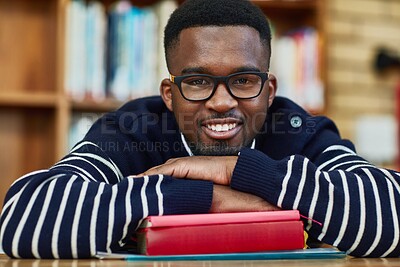 Buy stock photo African man, book and portrait at university, library and happy for studying, learning or development. Person, student and smile with laying at desk with research for assessment, exam or quiz in hall