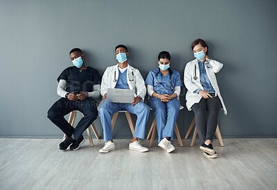 Buy stock photo Chairs, team and tired doctors by wall for interview or public health conference and training meeting. People, medical staff and line for patient rounds or daily briefing, review and exhausted.