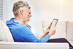 Happy mature couple browsing online on a digital tablet while relaxing together on a sofa at home