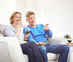 Happy mature couple drinking wine and eating popcorn while watching tv and relaxing together on a sofa at home
