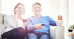 Happy mature couple drinking wine and eating popcorn while watching tv and relaxing together on a sofa at home