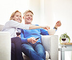 Happy mature couple drinking wine and eating popcorn while watching tv and relaxing together on a sofa at home