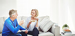 Mature couple drinking tea and eating sandwiches while having a conversation and relaxing together on a sofa at home