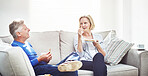Mature couple drinking tea and eating sandwiches while having a conversation and relaxing together on a sofa at home