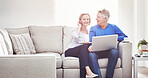 Mature couple browsing online on a laptop while relaxing together on a sofa at home