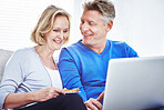 Mature couple browsing online on a laptop while relaxing together on a sofa at home