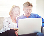 Mature couple browsing online on a laptop while relaxing together on a sofa at home