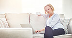 Mature woman drinking coffee and browsing online on a laptop while relaxing alone on a sofa at home