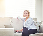 Mature woman drinking coffee and browsing online on a laptop while relaxing alone on a sofa at home