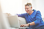 Mature man browsing online on a laptop while relaxing alone on a sofa at home