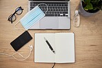 Office desk layout of laptop keyboard, face mask, hand sanitiser, glasses, smartphone with earphones and notebook with pen during the covid-19 pandemic 