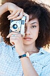Young mixed race woman with curly hair taking creative photos on a vintage retro film camera. One female photographer looking in viewfinder while capturing pictures as a hobby or profession on a shoot