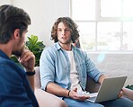 young man uisng laptop chatting to friend brainstorming ideas for project sitting on couch at home