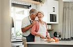 Senior couple in kitchen, cooking healthy food together and happy in retirement lifestyle. Elderly woman chopping vegetables with apron, old white man hug wife in home and love nutrition dinner meal