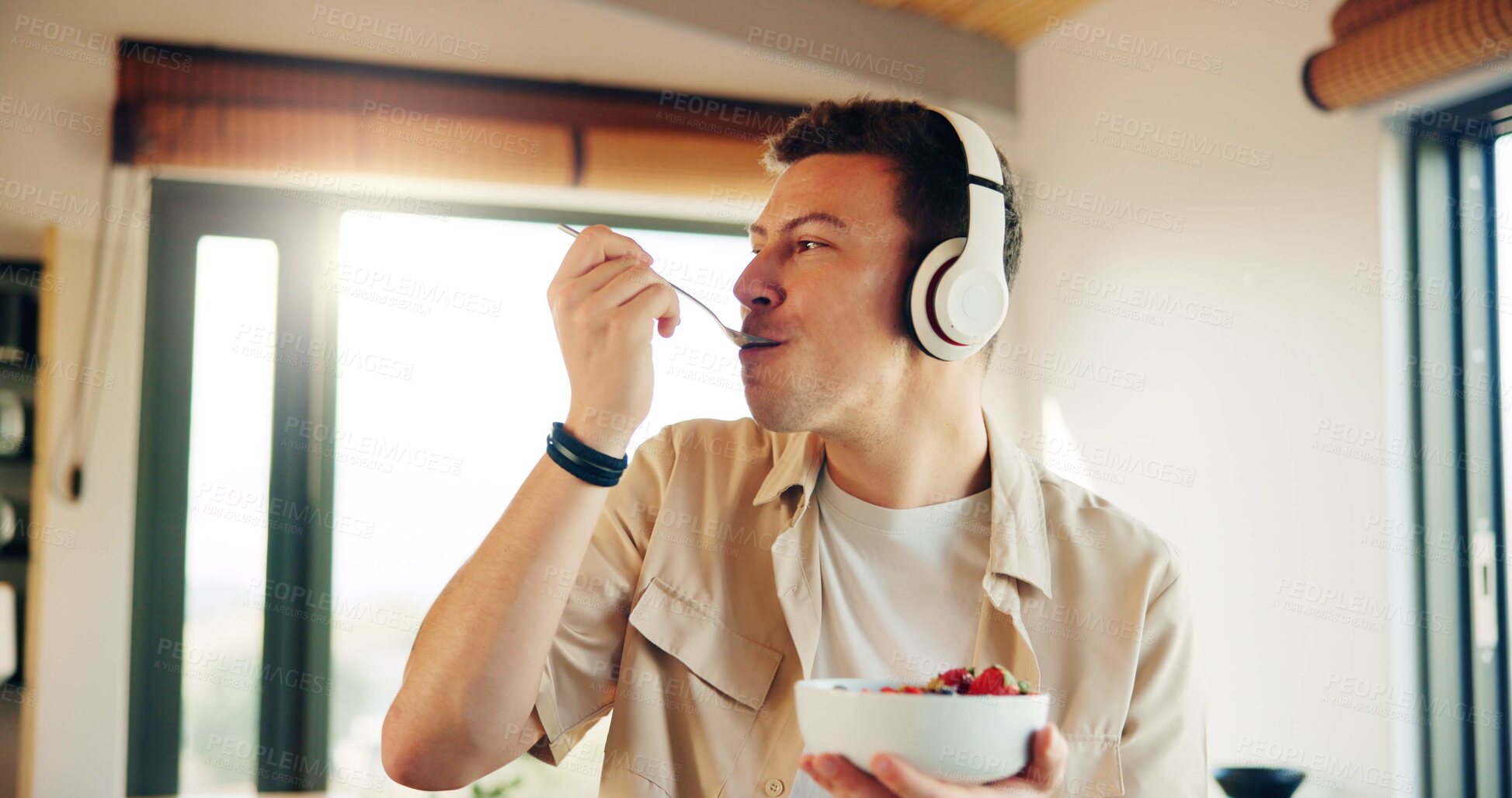 Buy stock photo Headphones, eating and man with breakfast in kitchen  listening to podcast in morning for self care. Audio tech, health and male person enjoying fruit salad for diet, nutrition or wellness in home.