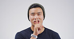 Happy, portrait and man in studio with secret, gossip or confidential hand gesture for privacy. Quiet, smile and Asian male person with finger on lips for silence or noise control by white background