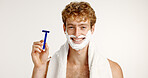 Portrait, shave cream and man with razor, smile and facial product on white studio background. Face, happy person and model with towel, beard care and wellness with hair removal, beauty and grooming