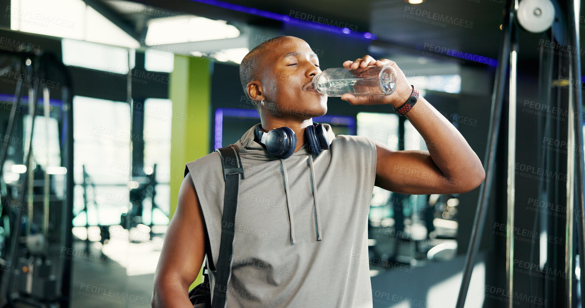 Buy stock photo Thirsty, man and drinking water in gym, break and nutrition for healthy body, exercise and wellness. Rest, athlete and black person with liquid for hydration, workout and headphones in fitness center