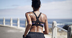 Back view, black woman and running with fitness on promenade for workout, exercise or training. Active, female person or runner with earphones for cardio marathon, health or outdoor wellness by beach