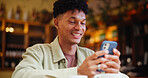 Man, phone and texting with smile at cafe with contact, typing and streaming on web at restaurant. Person, smartphone and click with chat, search and check post with social media at coffee shop