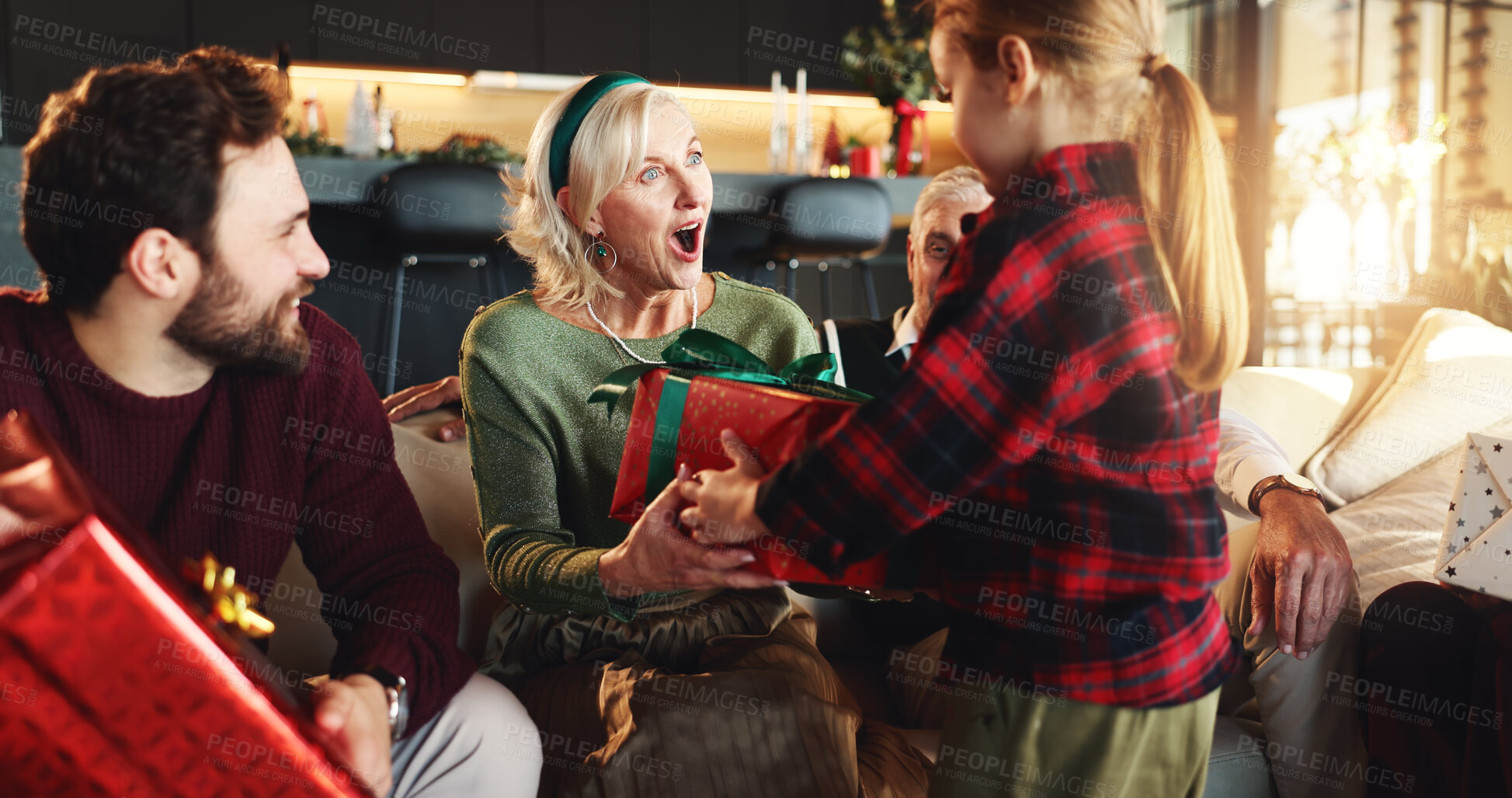 Buy stock photo Christmas, gift and surprise with family on sofa for holiday season, bonding and support. Festive celebration, shocked and xmas present with grandmother and child in living room of home for love