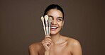 Happy woman, makeup and beauty with brushes in studio for cosmetics on a brown background. Female person, model or smile with skincare tools for cosmetology, foundation or blending shade on space