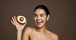 Woman, avocado and happy in studio for skincare, laugh and nutrition for beauty by background. Girl, model and thinking with food for wellness benefits, fruit diet and excited for results with glow