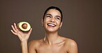 Girl, avocado and happy in studio for skincare, laugh and nutrition for beauty by background. Woman, model and thinking with food for wellness benefits, fruit diet and space for results with glow
