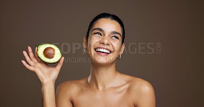 Buy stock photo Girl, avocado or happy in studio for skincare, laugh and nutrition for beauty by brown background. Woman, model or thinking with food for wellness benefits, fruit diet and space for results with glow