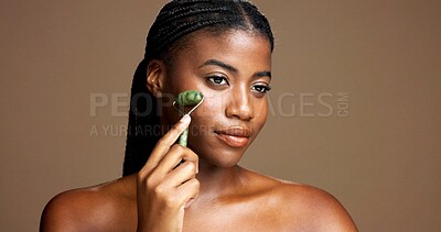 Buy stock photo Beauty, skincare and girl with jade roller in studio for depuffing, facial massage and skin glow. Mockup, black woman or cosmetics tool on brown background for lymphatic drainage, routine or radiance