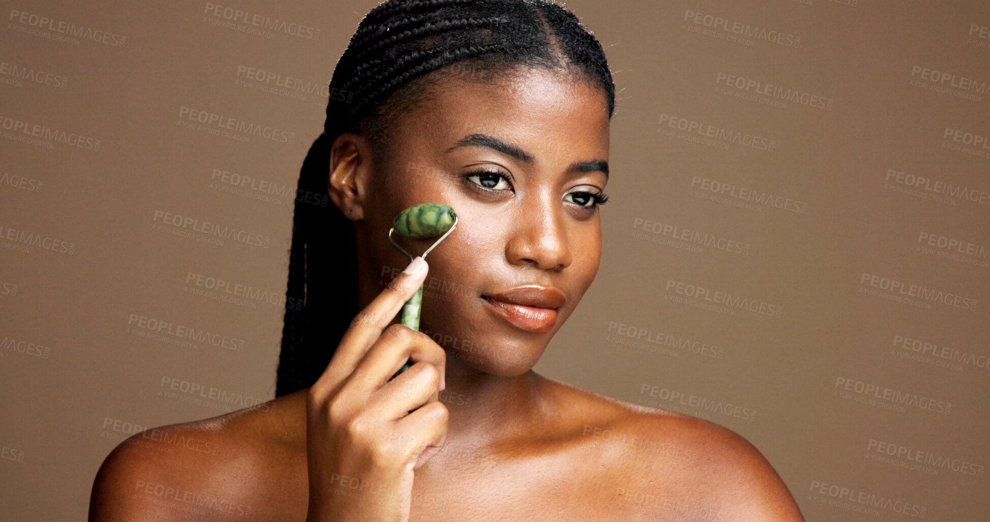 Buy stock photo Beauty, skincare and girl with jade roller in studio for depuffing, facial massage and skin glow. Mockup, black woman or cosmetics tool on brown background for lymphatic drainage, routine or radiance