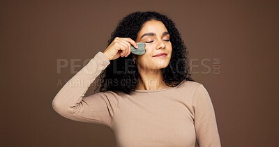 Buy stock photo Beauty, skincare and woman with gua sha in studio for facial care, detox and lymphatic drainage. Dermatology, spa and person with jade tools for anti aging, massage or smooth skin on brown background