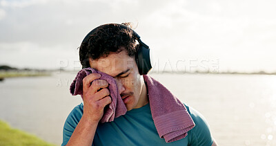 Buy stock photo Tired man, sweat or fitness with towel or headphones at lake for intense workout, break or recovery. Active, male person or dry with cloth for physical activity, exercise or outdoor training at river