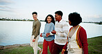 Walking, happy and friends outdoor by lake on vacation, getaway or weekend trip together. Talking, bonding and group of young people in nature for reunion, gathering or catch up on holiday travel.