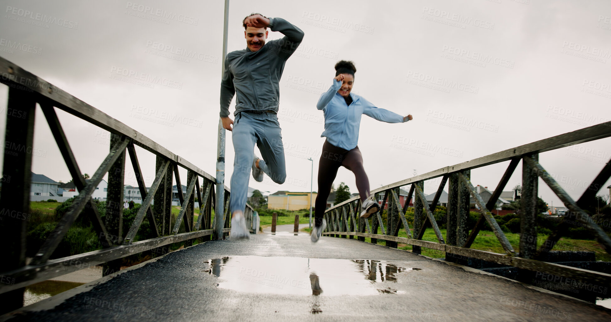 Buy stock photo Exercise, running and couple with jumping on bridge for pace training, winter workout and teamwork. Fitness, puddle and people with cardio outdoor for race endurance, marathon competition and support