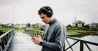 Buy stock photo Headphones, athlete or man on bridge with phone for workout, tracking exercise or song. Lake, outdoor or runner on mobile app in city for running progress, music playlist and fitness podcast audio