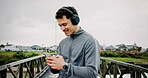 Headphones, runner or man on bridge with phone for workout, tracking exercise and song. Lake, smile or athlete on mobile app in city for running progress, music playlist and fitness podcast audio