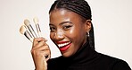 Happy, black woman and portrait with makeup brushes in studio for beauty on a white background. Face, female person or African model with smile or cosmetics tools for foundation or skin application