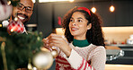 Couple, help and christmas tree decoration in home for festive tradition, preparation or support. Night, african people and happy with bauble ornaments in lounge for xmas eve aesthetic or celebration