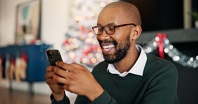 Buy stock photo Christmas, black man and typing with phone in home for holiday text, season greeting and chat. Happy, person and relax with smartphone in house for online shopping or search donation site for charity