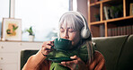 Senior woman, drinking coffee and headphones on sofa with smile, audio or inspiration in retirement home. Person, relax and listen to music with subscription, streaming or tea in lounge at house