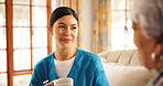 Caregiver, coffee and discussion in nursing home with patient, support feedback and relax on sofa. Assisted living, senior woman and nurse in retirement center with drink, bonding and daily checkup