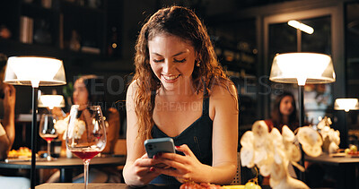 Buy stock photo Happy, woman and phone with texting in restaurant for online dating app, dinner planning and chat. Night, wine and person with smartphone in diner for waiting, social networking and typing location