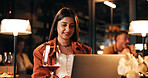Laptop, wine and woman in restaurant at night with online blog for hospitality review with freelance. Remote work, drink and female author with computer for writing book chapter at luxury cafe.