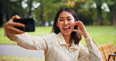 Buy stock photo Smile, Japanese woman and bench with selfie at park for expression, emotion or love in nature. Traveler, person and user with hand, heart sign and emoji for photography, picture or outdoor memory