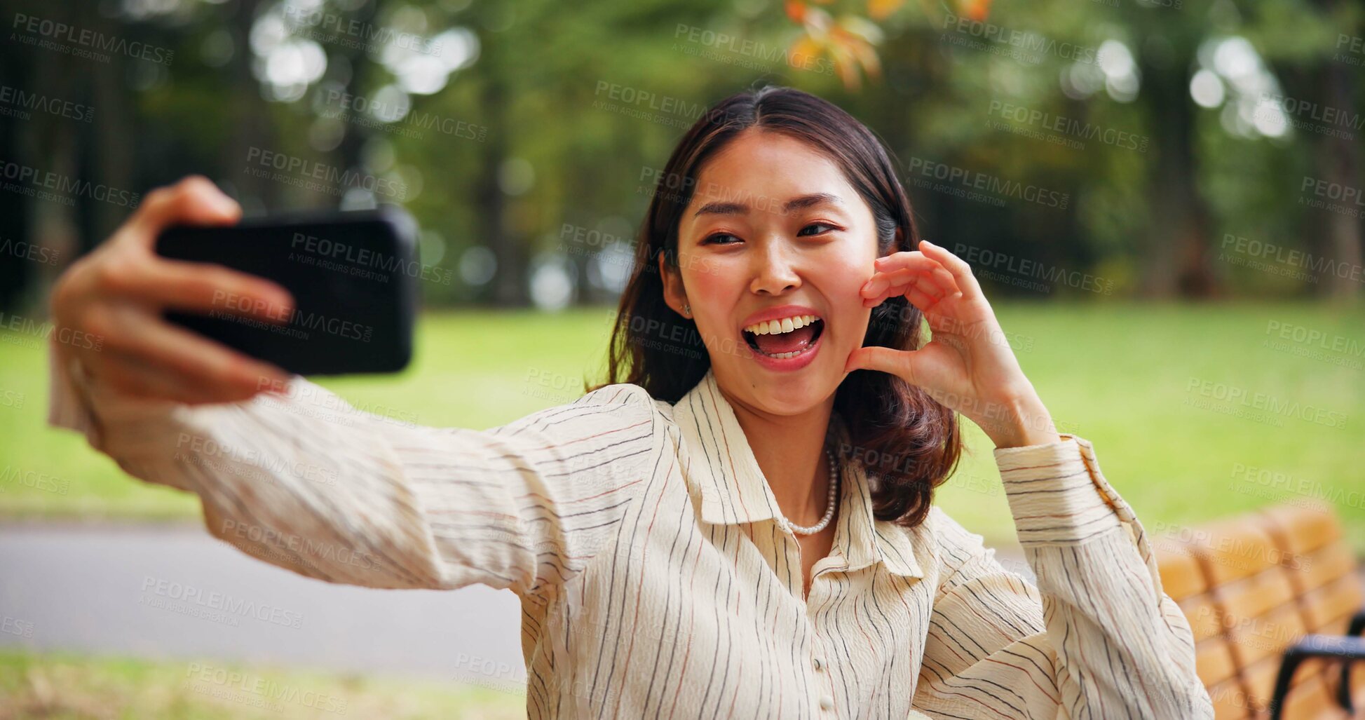 Buy stock photo Smile, Japanese woman and bench with selfie at park for expression, emotion or love in nature. Traveler, person and user with hand, heart sign and emoji for photography, picture or outdoor memory