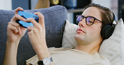 Buy stock photo Home, headphones and man with smartphone, video game and streaming service with audio tech. Apartment, relax and person with cellphone, entertainment or playing with app, gaming or virtual sports