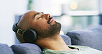 Relax, headphones and eyes closed with man on sofa for streaming service, calm audio and ambient sound. Guided podcast, white noise and peace playlist with person in living room of home for break