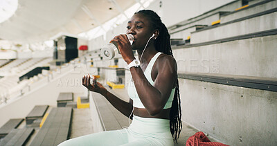 Buy stock photo Stadium, black woman and drink with water bottle for fitness, hydration or running break. Outdoor, athlete person and health with earphones for training podcast, exercise and music for workout rest