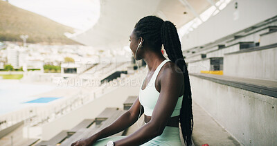 Buy stock photo Earphones, sports and black woman on break with music, playlist or radio for workout rest. Audio tech, fitness and African athlete listening to album in stadium for exercise, training or practice.